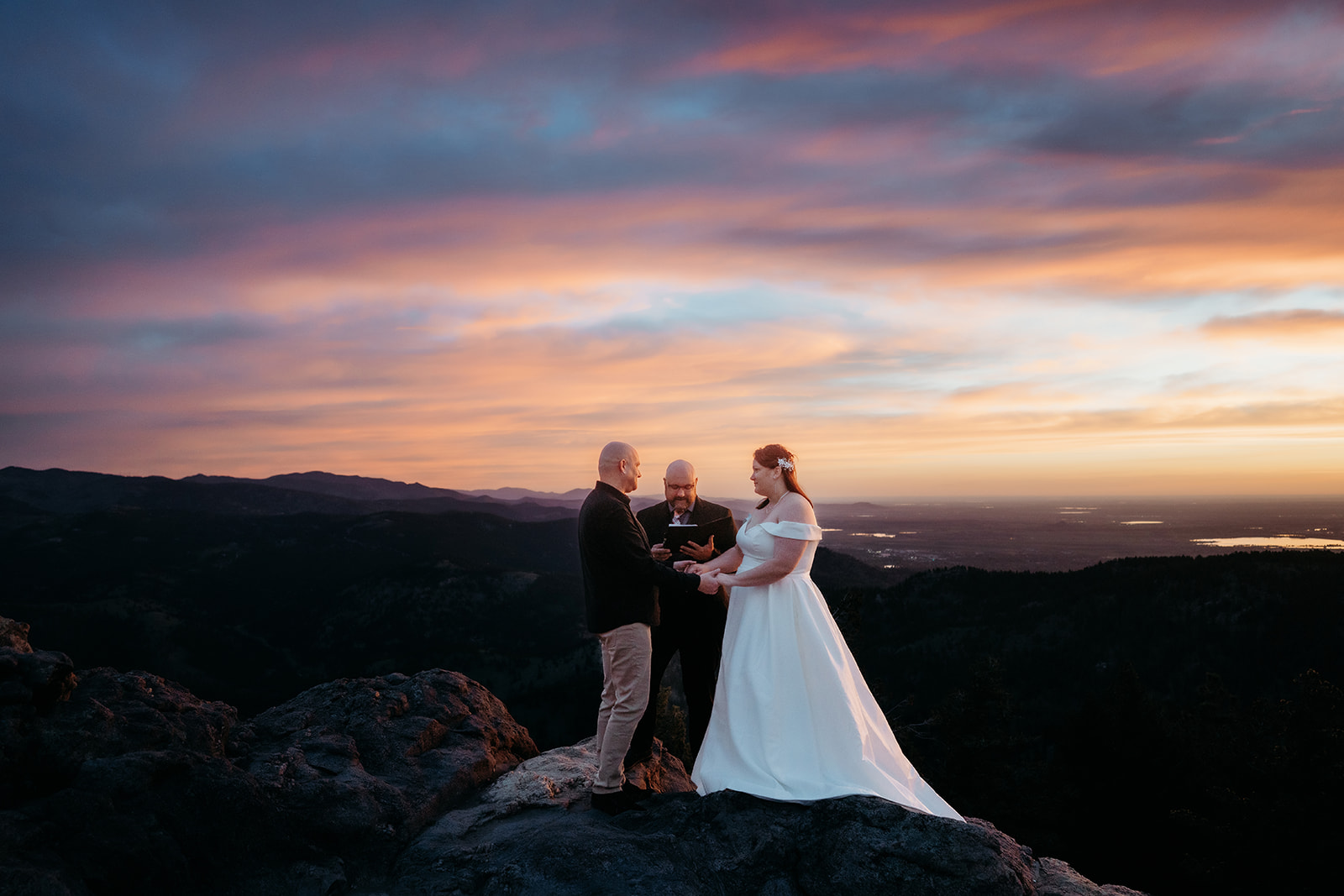 Exchanging vows on a dramatic mountaintop, the couple stands with their officiant under a vibrant Colorado sky during their elopement.