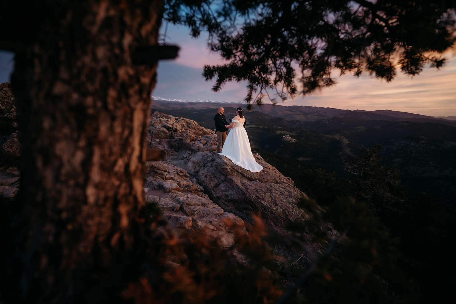 Framed by a tree in the foreground, the couple stands alone on a rocky cliff during their intimate Colorado elopement ceremony.