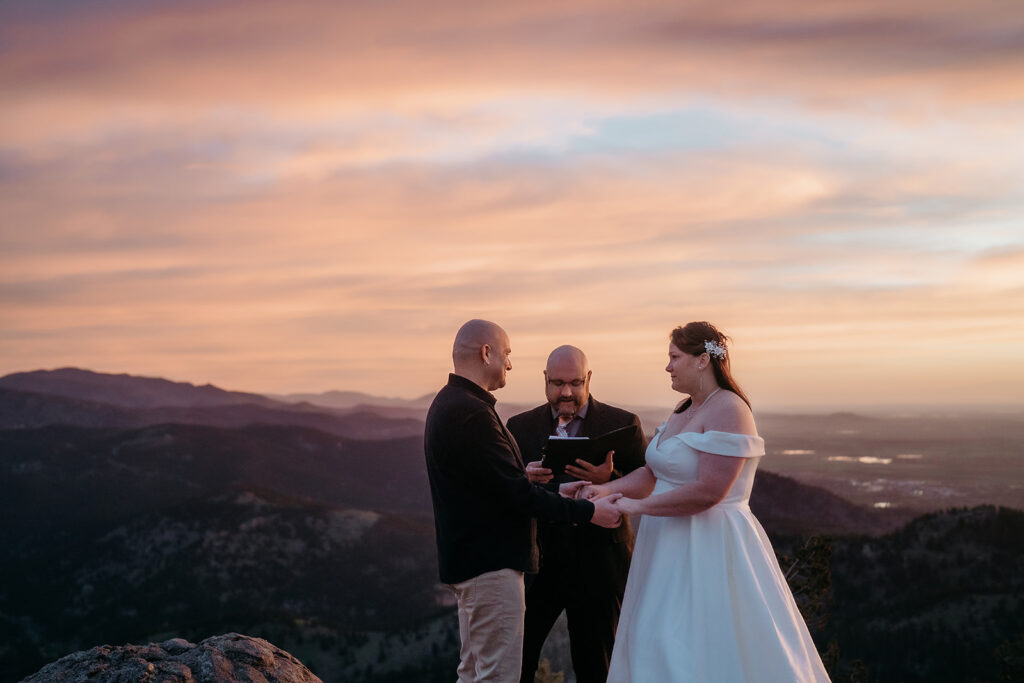 Golden hour elopement ceremony as the couple exchanges vows on a mountaintop, perfectly framed by their elopement photographer Colorado.