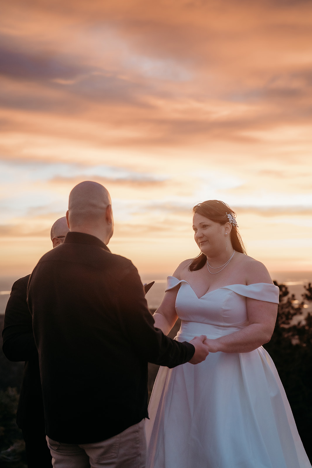 Emotional vow exchange at sunset, with warm light spilling across the bride’s face and groom holding her hands.