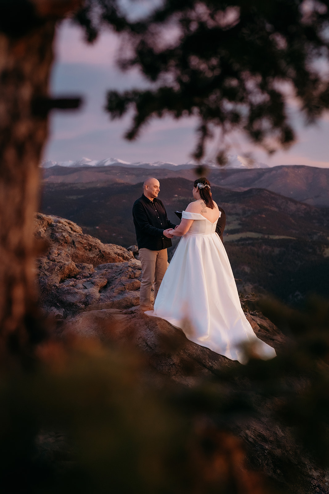 Elopement ceremony on a mountain ledge, framed by trees and deep shadows, captured by a storytelling-focused elopement photographer Colorado.