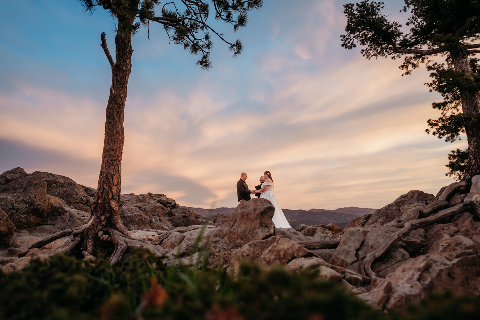 Wide view of a mountaintop ceremony framed by trees and rocks, captured at golden hour by an elopement photographer Colorado couples trust.