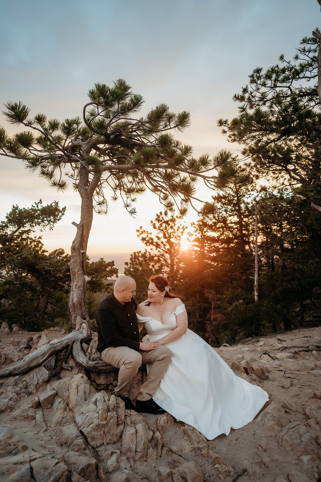 Sitting beneath a pine tree at sunset, the couple shares a laugh, soaking in the calm after their vows—pure mountain magic.