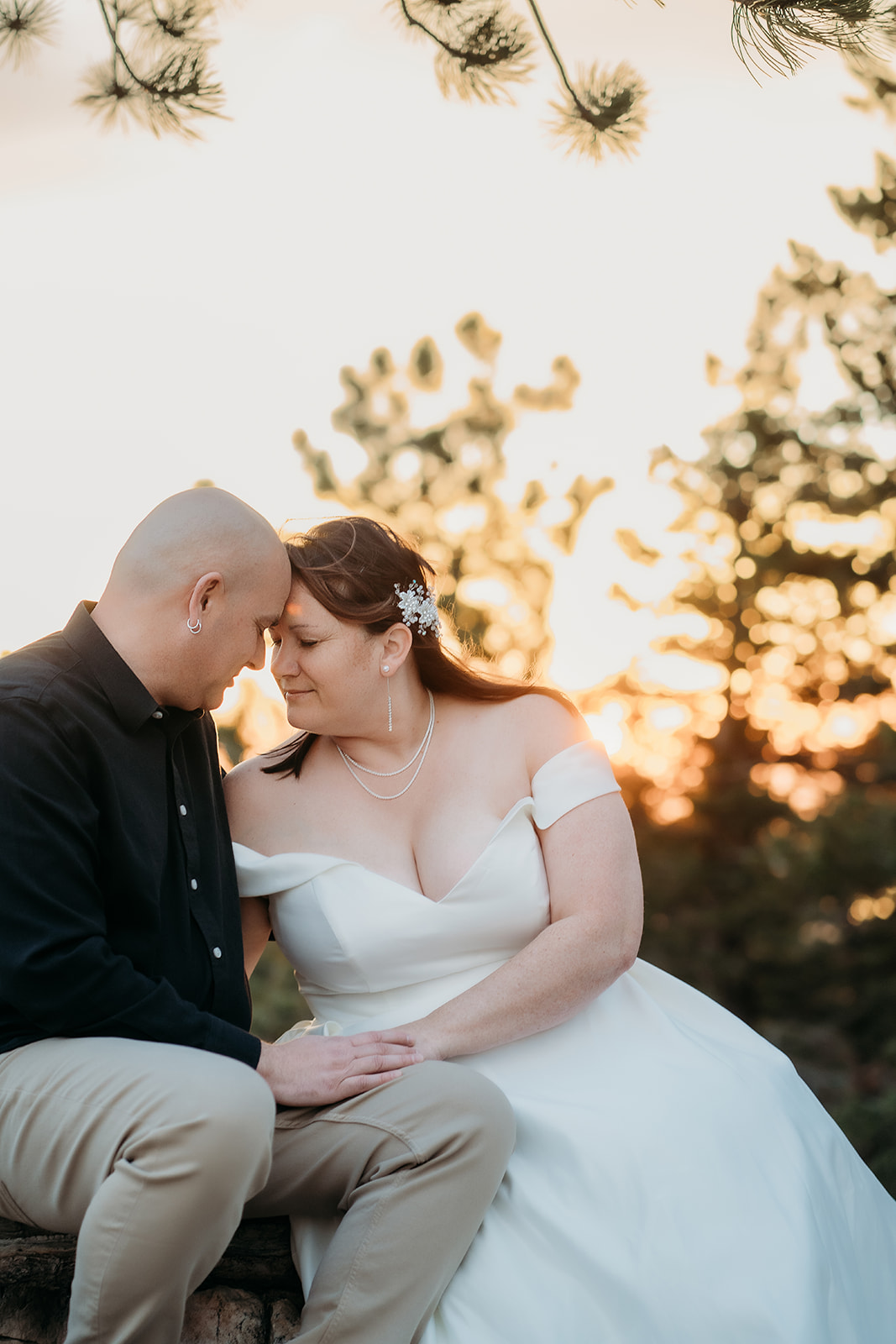 Foreheads pressed together at golden hour, the couple shares a quiet moment with the softest smiles and evening light behind the trees.