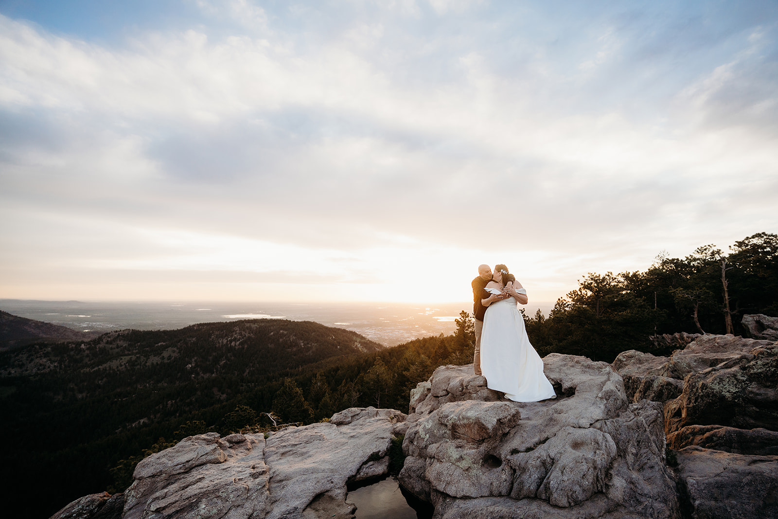Standing on a rugged cliff, the couple embraces as the sun dips low over the Colorado horizon—captured by their elopement photographer.