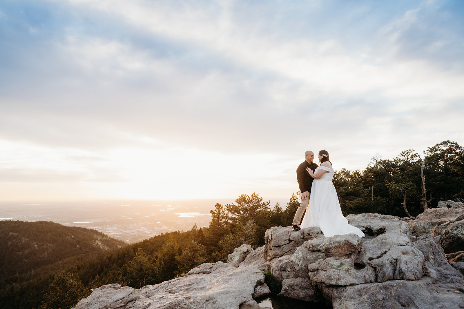 High on a rocky overlook, the newlyweds share a quiet hug as the sunset stretches across the landscape behind them.