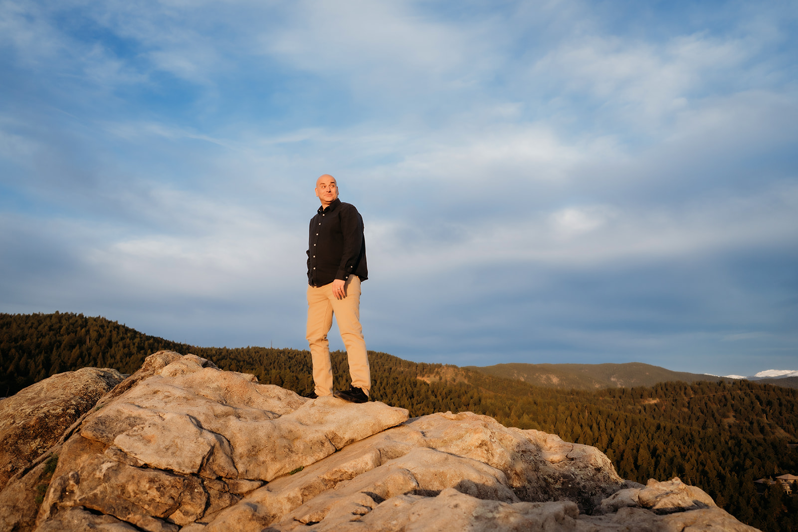 Groom stands solo on a rock ledge, lit by the warm setting sun and the endless Colorado landscape behind him.