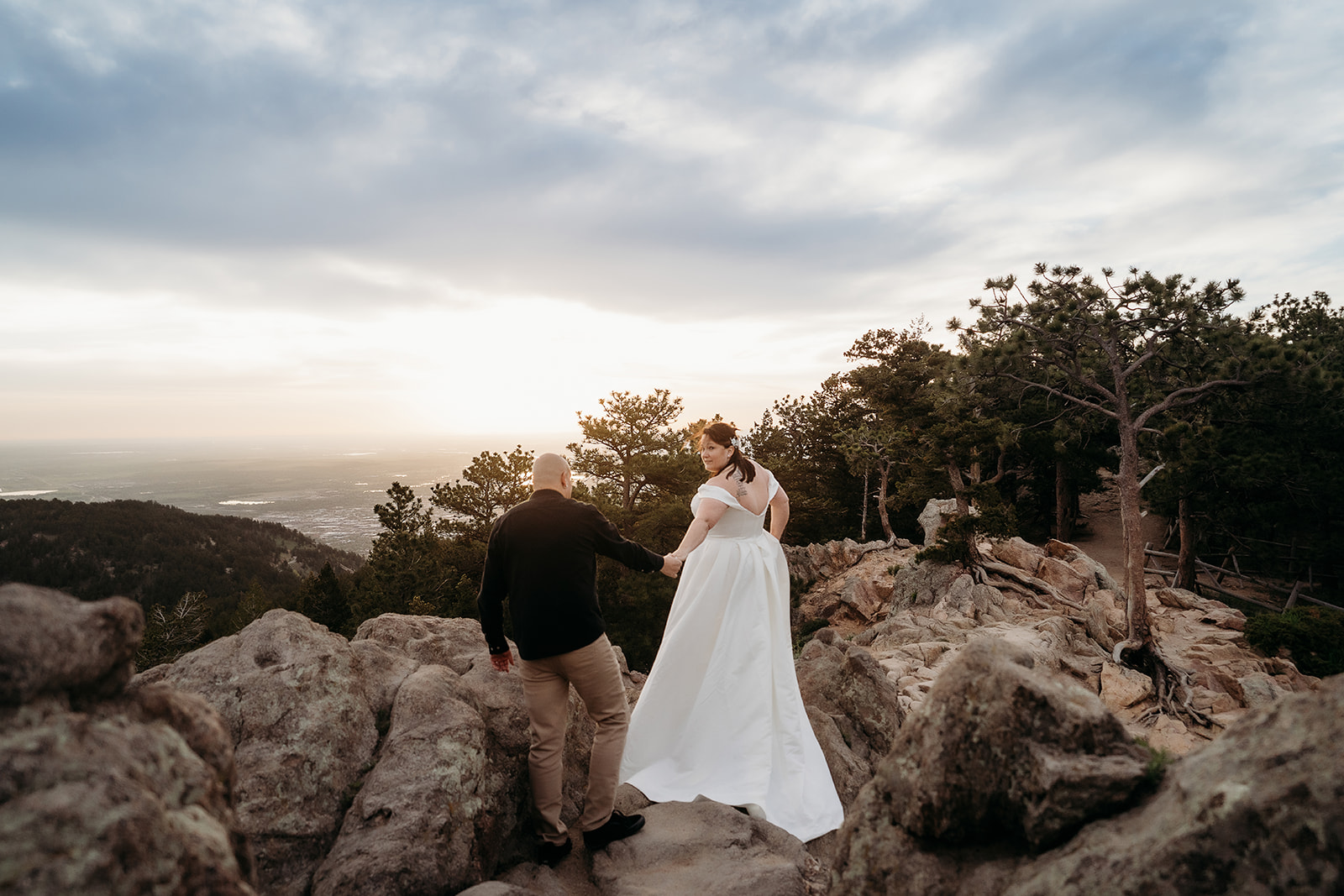 Walking hand-in-hand toward the horizon, the couple navigates rocky terrain at sunset, led by their elopement photographer Colorado.