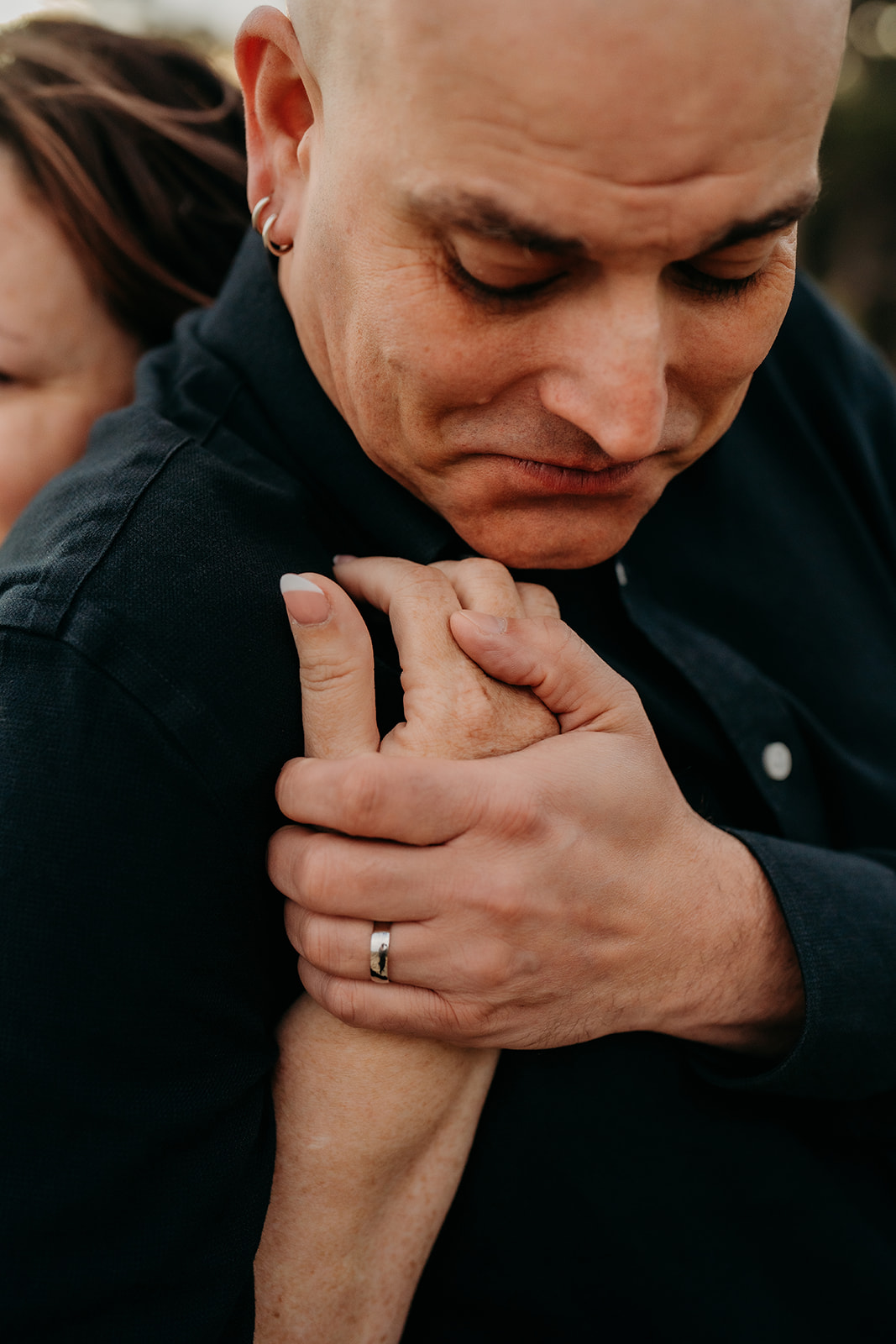 Close-up of the groom holding his partner’s hand gently against his chest, wedding band in focus in a quiet, emotional moment.