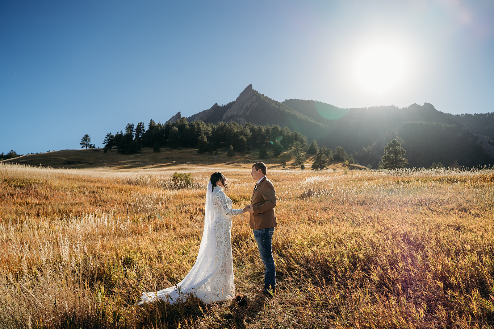 Couple stands hand-in-hand in a wide open field with dramatic Flatirons views and warm sunshine—an iconic Boulder elopement moment.