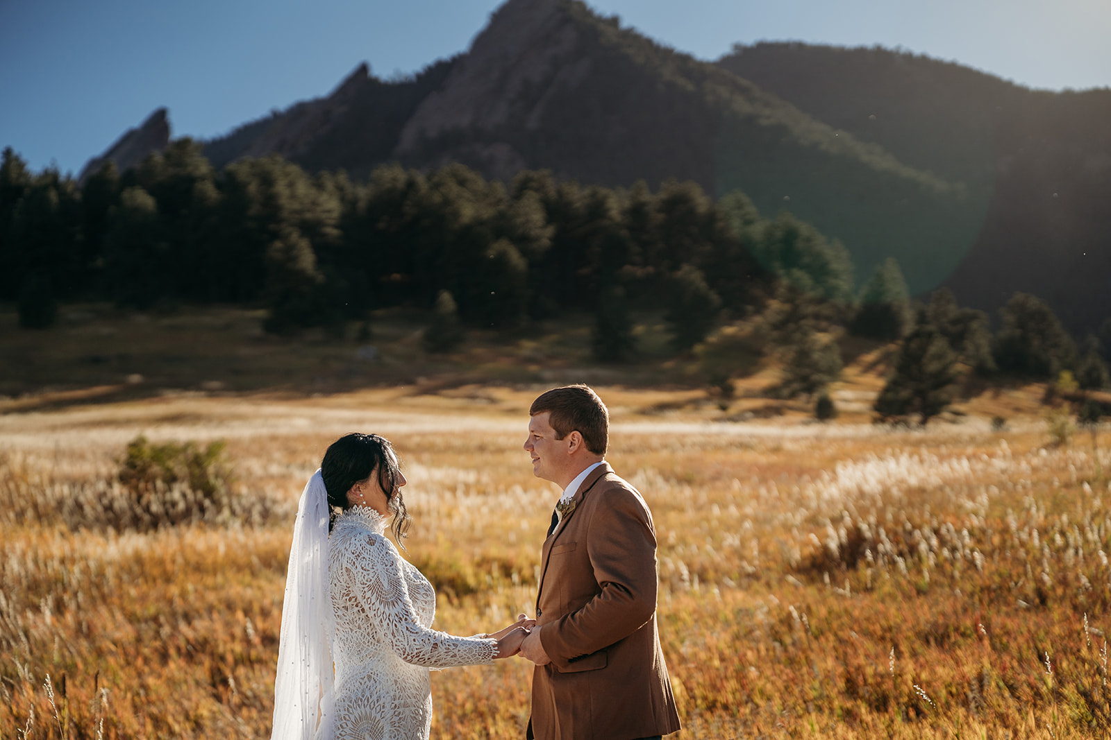 Bride and groom holding hands and smiling at each other in front of the Flatirons on their intimate Boulder elopement day.
