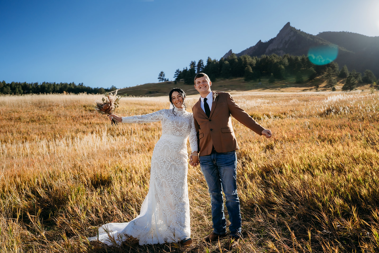Newlyweds celebrating in an open field with the Flatirons behind them, arms outstretched in pure joy during their Boulder elopement.