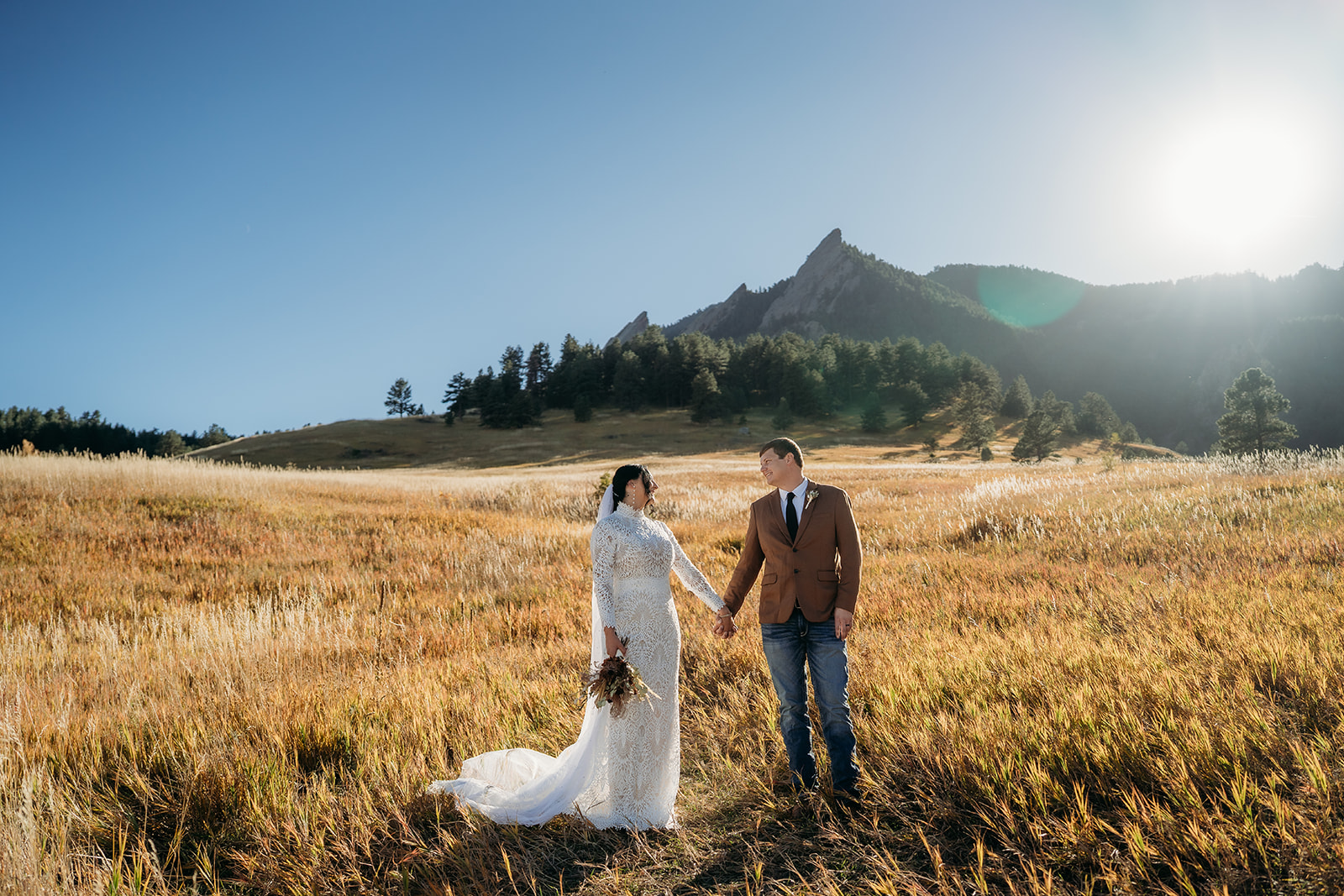 Bride and groom holding hands in a sunlit field with the Flatirons in the background, sharing a quiet moment during their Boulder elopement.