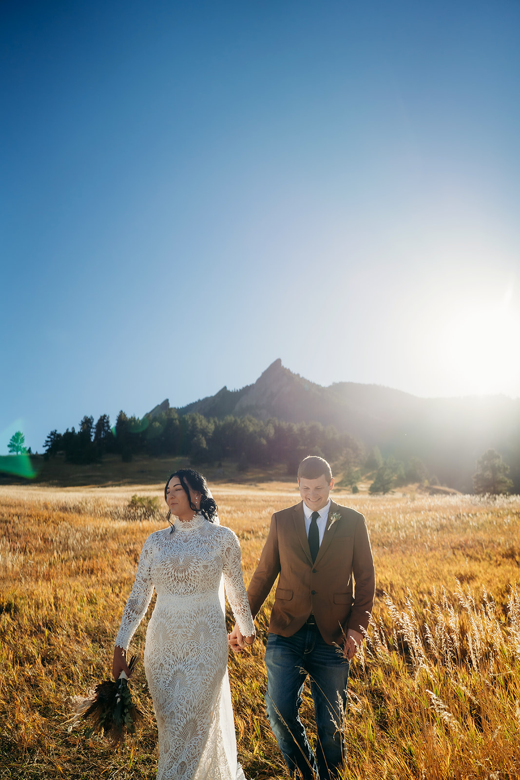 Bride and groom walking through a golden field with the Flatirons in the background during their relaxed Boulder elopement.