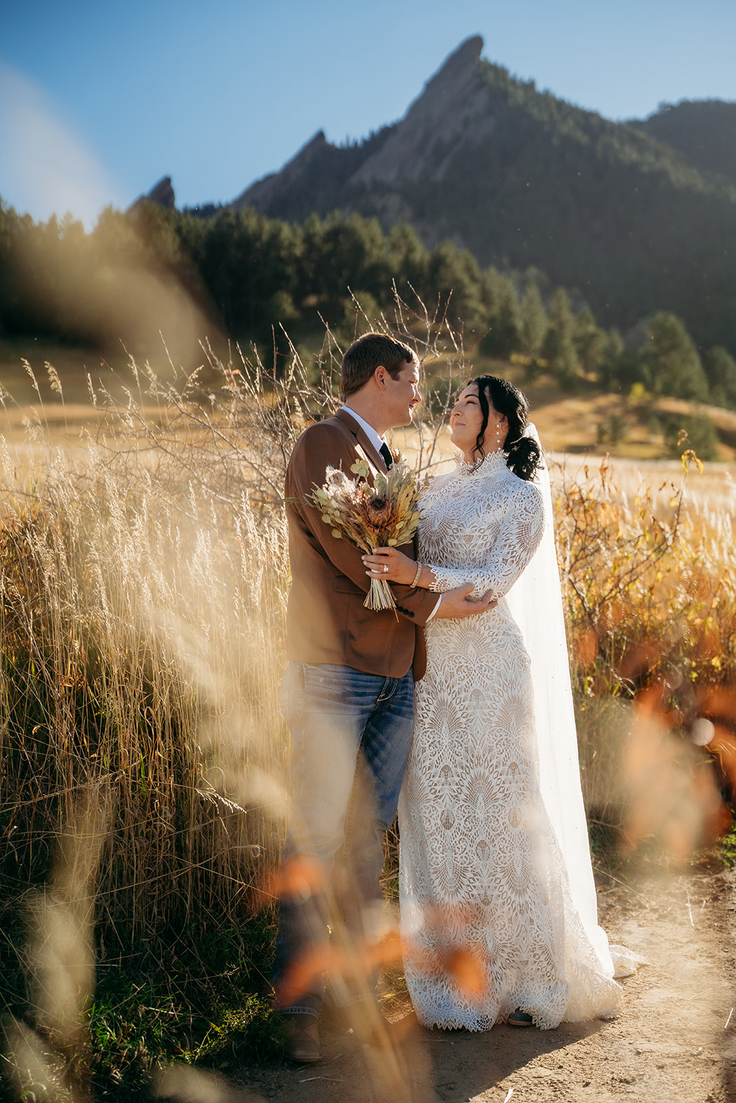 Bride and groom standing in a patch of tall grasses, lovingly facing each other with the Flatirons behind them during their Boulder elopement.