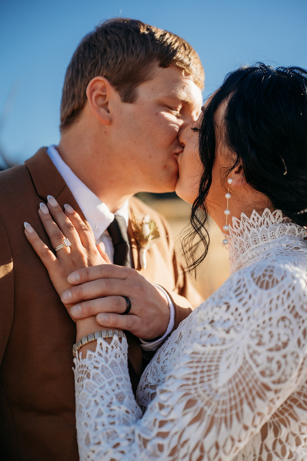 Close-up kiss between the couple, highlighting the bride’s lace gown, veil, and sparkling engagement ring.