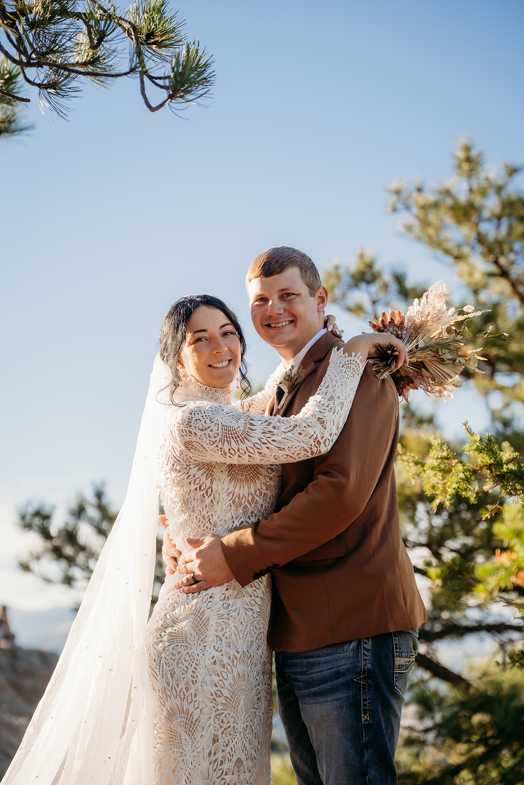 Couple posed in front of a rustic wooden fence, sunlight peeking through the trees during their Boulder elopement session.