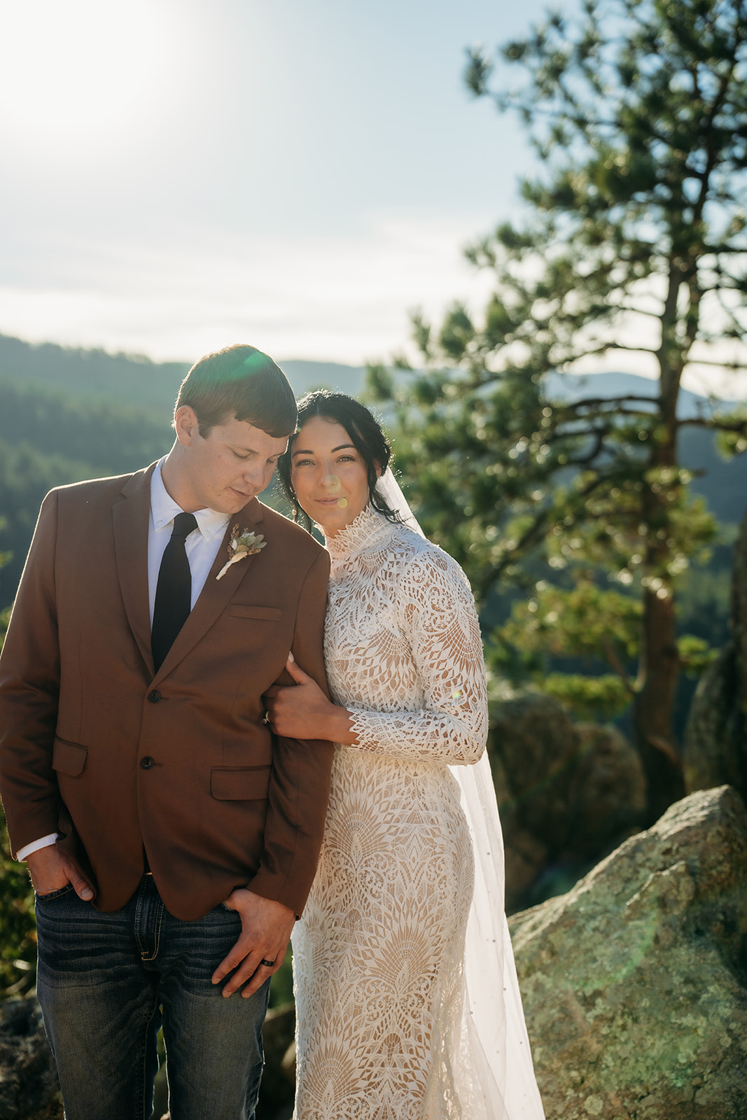Bride and groom stand together on a rocky overlook, surrounded by pine trees and soft mountain light during their Boulder elopement.