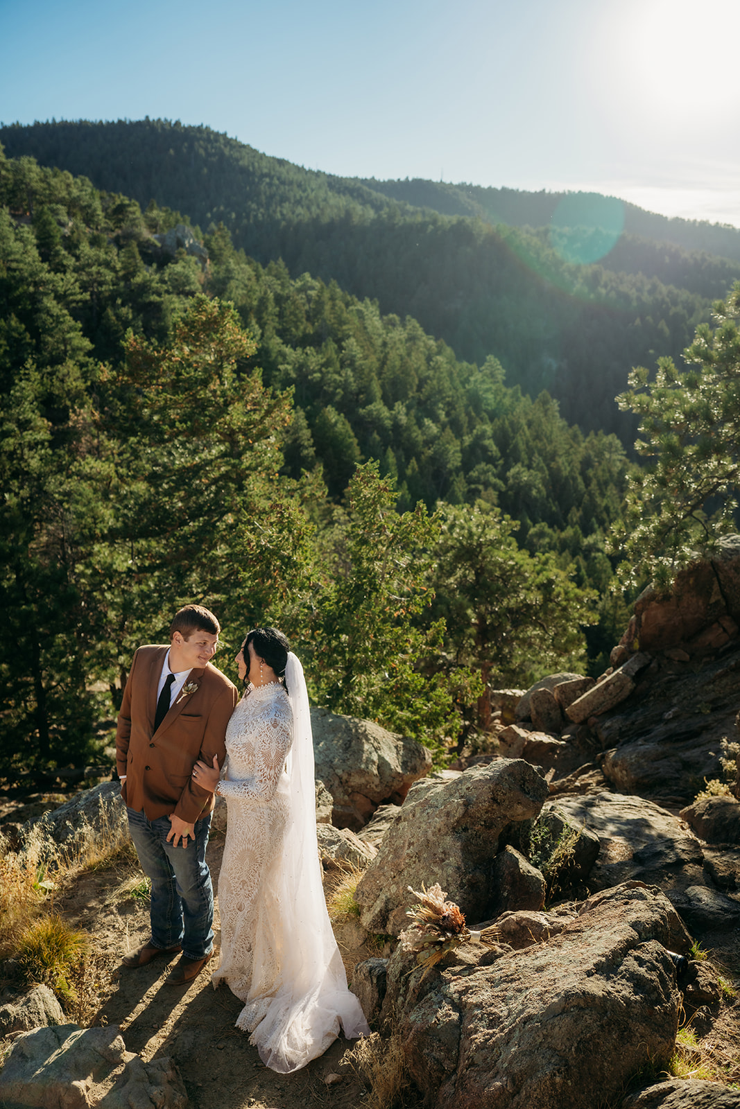 Bride and groom standing under pine trees on a rocky overlook, sharing a quiet kiss during their Boulder elopement ceremony.