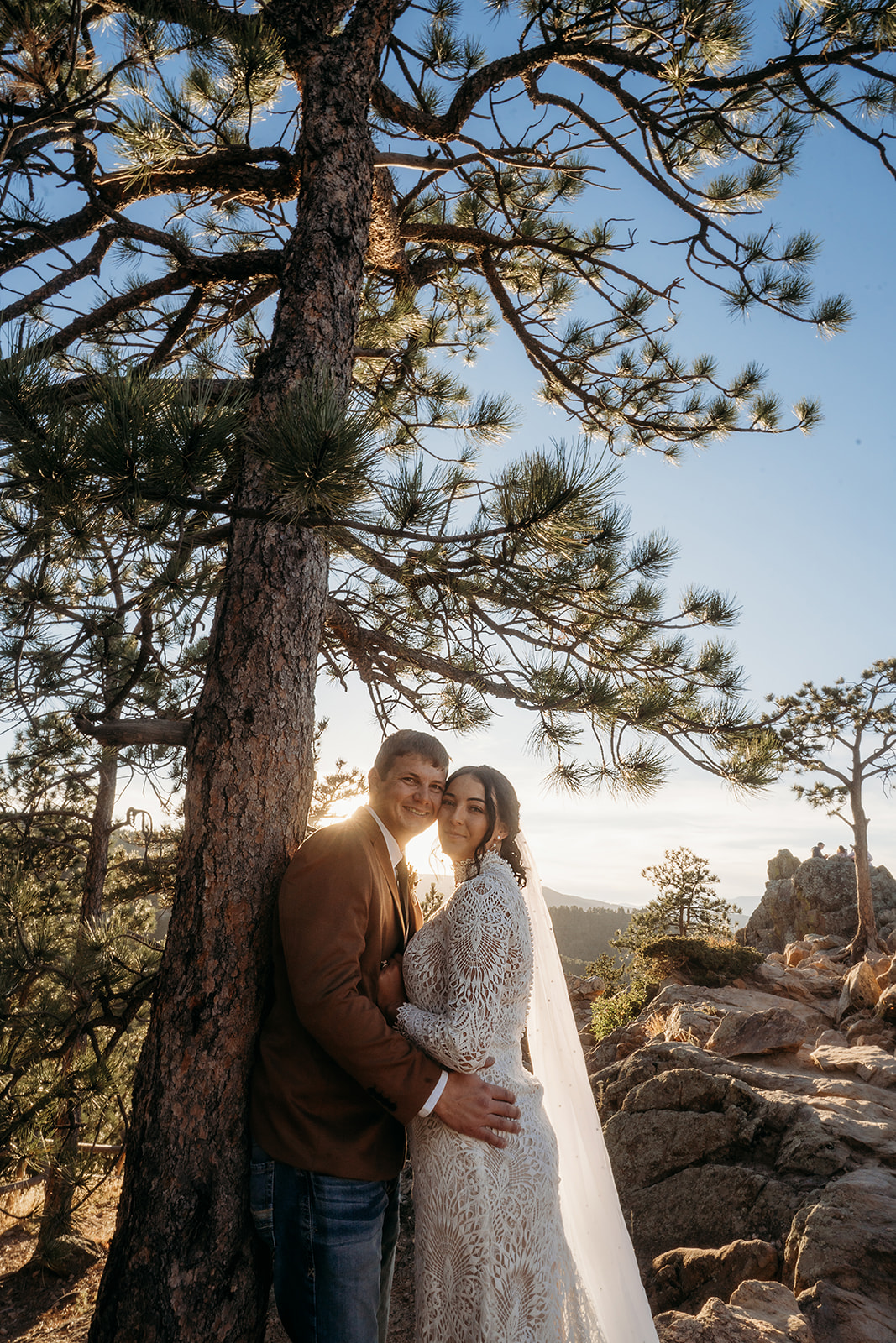 Wrapped in soft sunlight, the couple smiles beneath a tall pine on their Boulder elopement day, surrounded by rugged beauty.