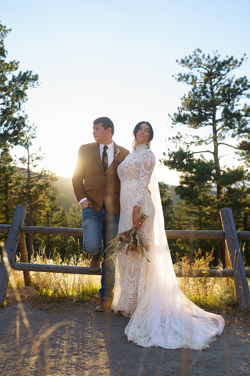 Bride and groom posing in front of a wooden fence at sunset, warm light streaming through the trees in true Colorado style.
