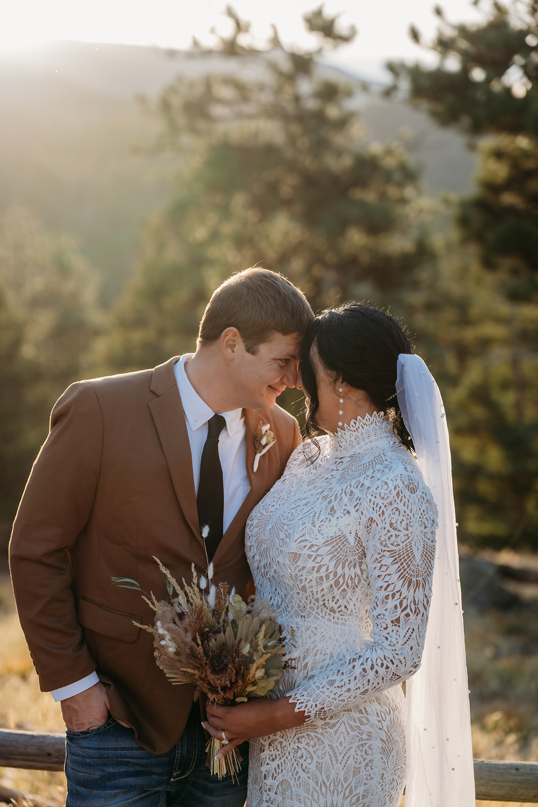 Close, quiet moment between the couple as they touch foreheads at golden hour with pine trees and mountains softly glowing behind them.