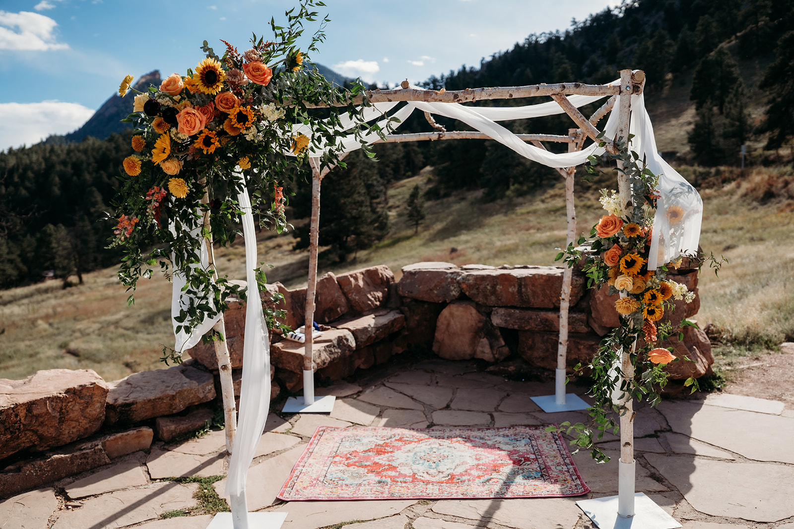 An empty floral ceremony arch decorated with sunflowers and greenery, set against mountain scenery before guests arrive for a Colorado wedding.