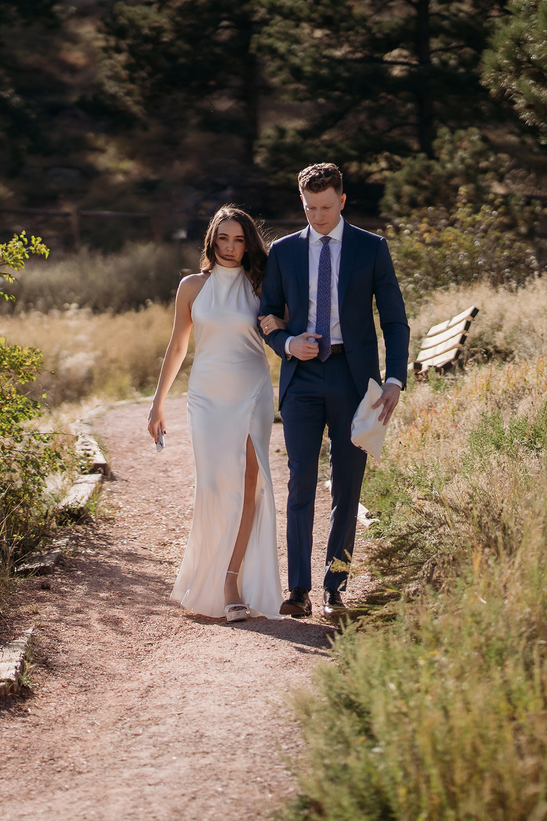 The newly married couple walking arm in arm along a dirt path, holding their ceremony papers and talking quietly after their Colorado wedding ceremony.