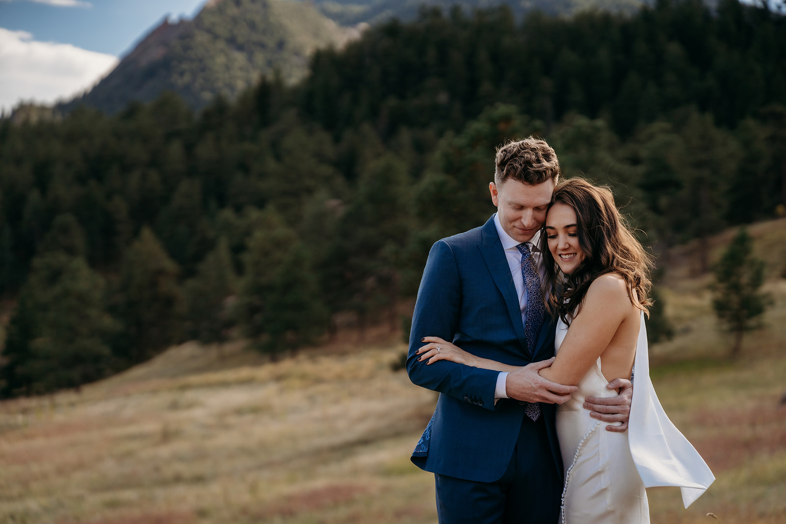 A bride and groom standing close and embracing in a mountain meadow, sharing a quiet moment during their Colorado wedding.