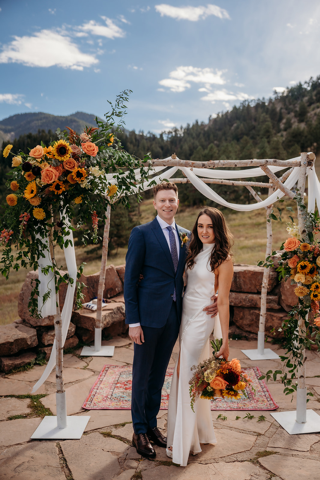 Bride and groom standing together at the alter while bride holds colorful sunflower bouquet before Colorado weddings to begin.