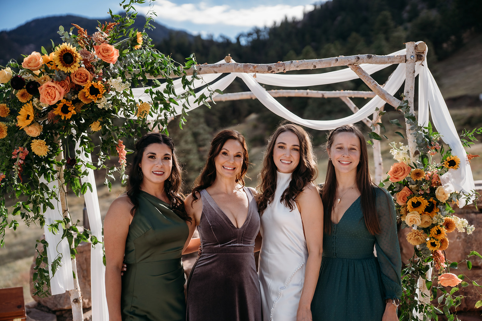 Four women standing together under a floral ceremony arch in the Colorado foothills, smiling during an intimate celebration of Colorado weddings.