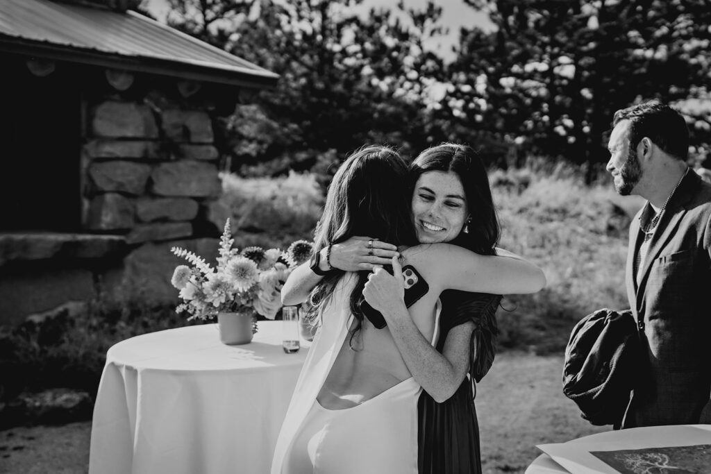A black and white moment of two women hugging tightly after the ceremony, smiling during an emotional moment at a Colorado wedding.