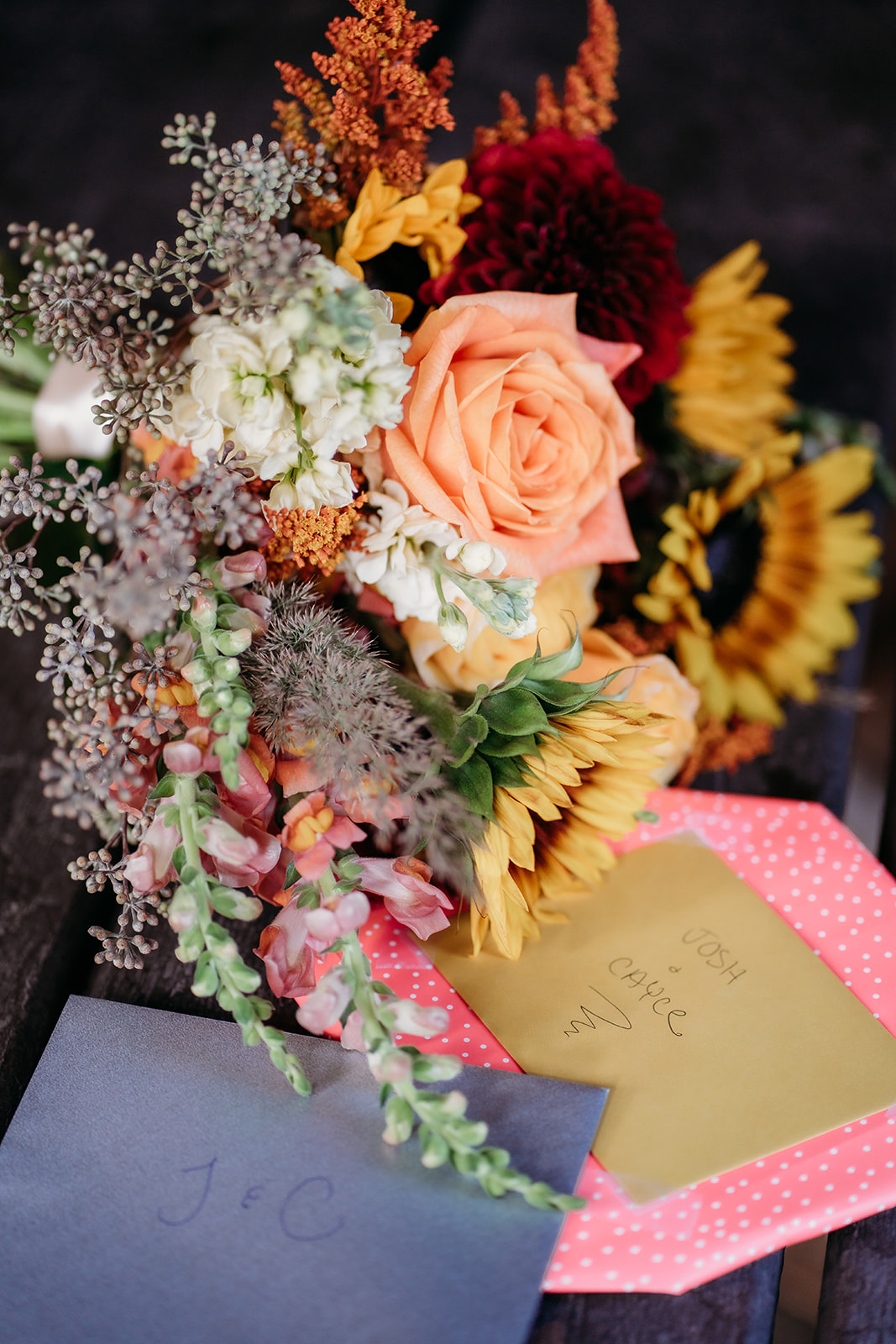 A detailed flat lay of a colorful fall wedding bouquet resting beside handwritten cards and envelopes during an intimate Colorado wedding.