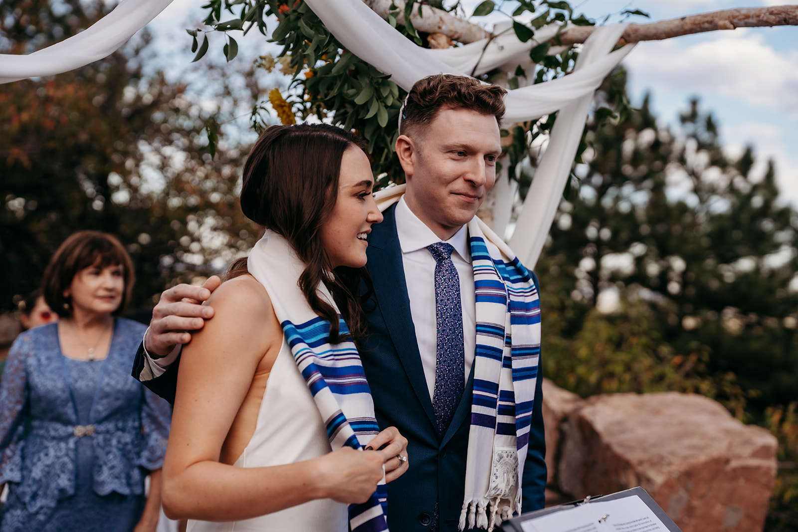 The bride and groom walking arm in arm after the ceremony, wearing ceremonial prayer shawls during a meaningful Colorado wedding tradition.