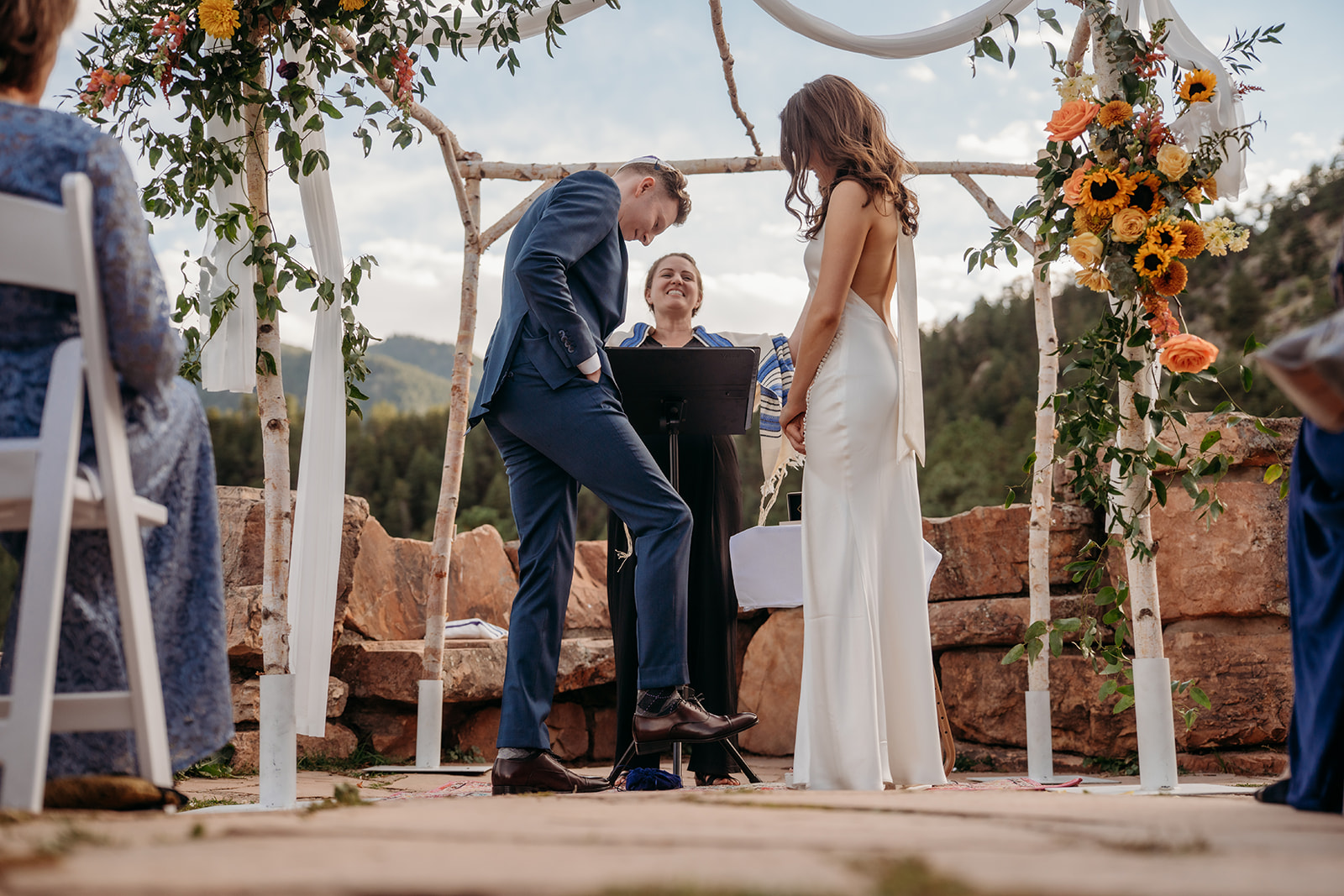 The couple standing at the altar with their officiant during an outdoor mountain ceremony, sharing a lighthearted moment during their vows.