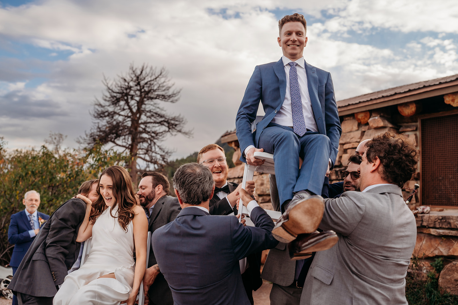 The groom lifted into the air on chairs by guests during a lively hora dance at an outdoor Colorado wedding celebration.