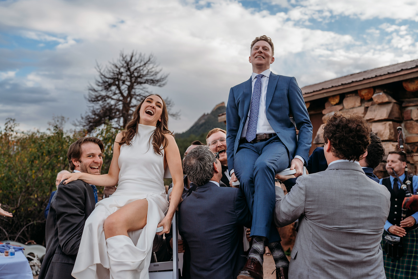 The bride and groom lifted into the air on chairs during the hora, laughing joyfully as guests celebrate around them at a Colorado wedding.