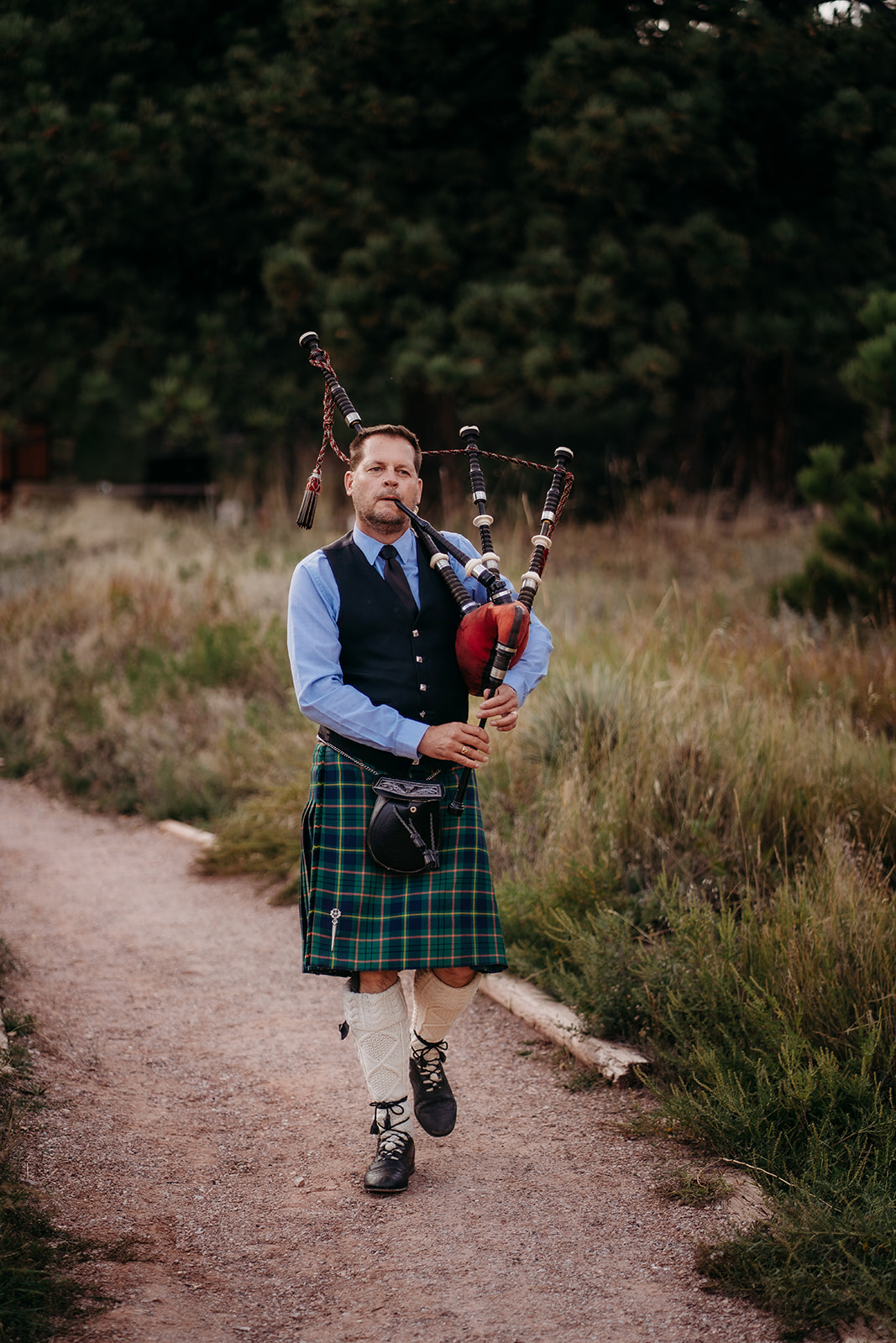 Bagpiper walking on trail while playing his instrument before the wedding reception is to begin.