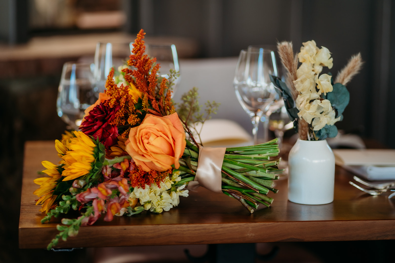 A fall wedding bouquet with sunflowers and warm-toned florals resting on a wooden table at a Colorado wedding reception.