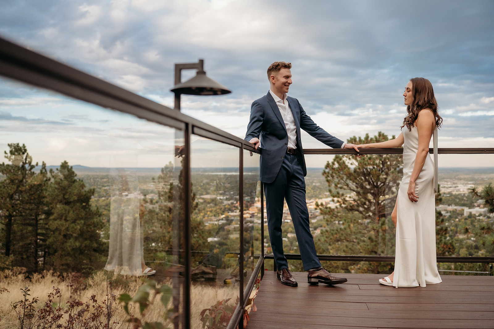 A couple holding hands on a wooden deck with sweeping mountain and city views during an intimate Colorado wedding celebration.