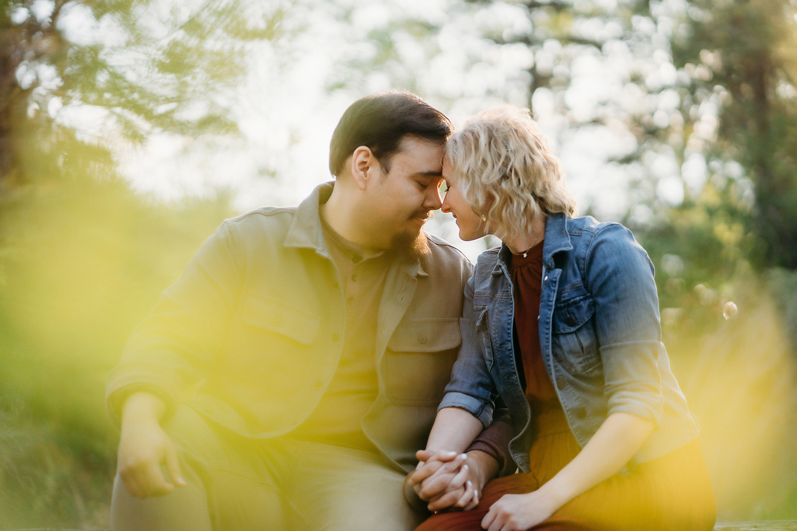 A soft and intimate forehead-to-forehead moment as the couple holds hands, framed by dreamy yellow light.