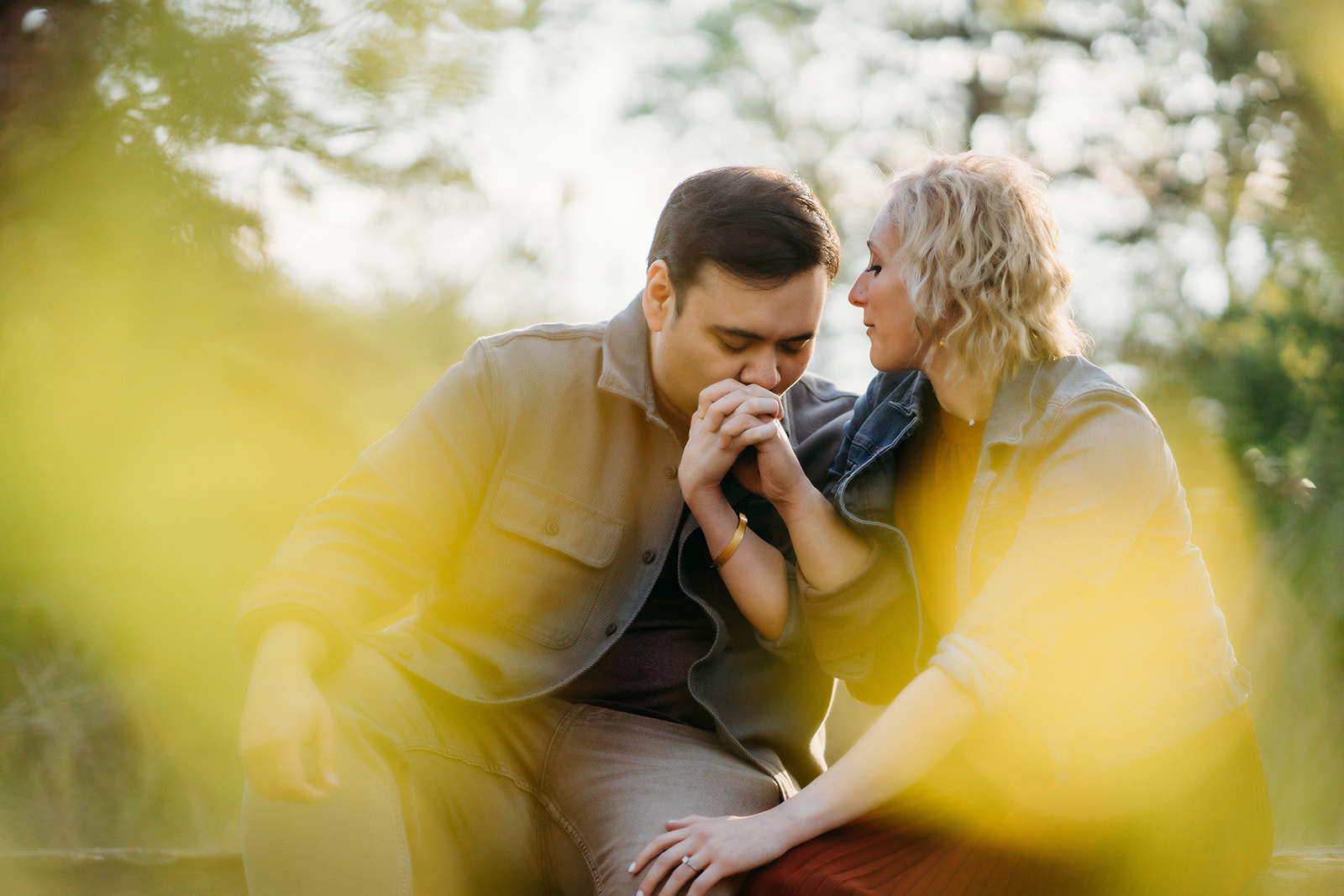 A quiet, emotional moment as a man kisses his partner’s hand, framed by soft yellow light—Denver engagement photographer.