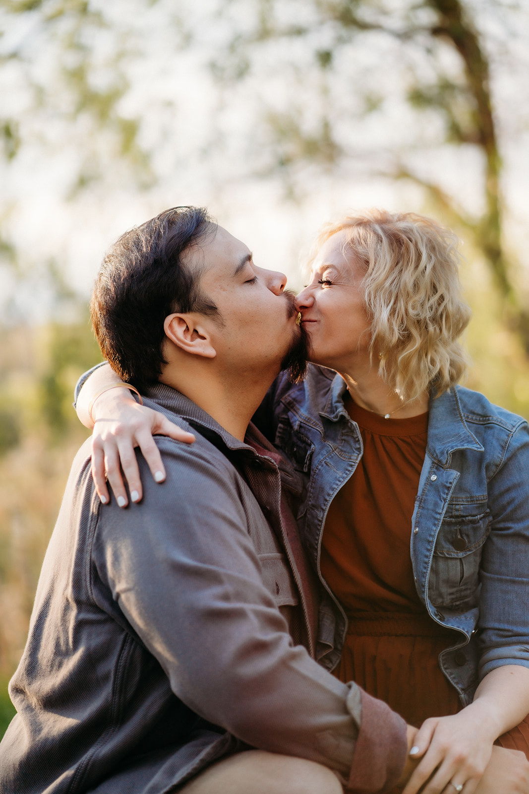 A woman leans in to kiss her partner, arms around his neck, surrounded by warm, late-afternoon light.
