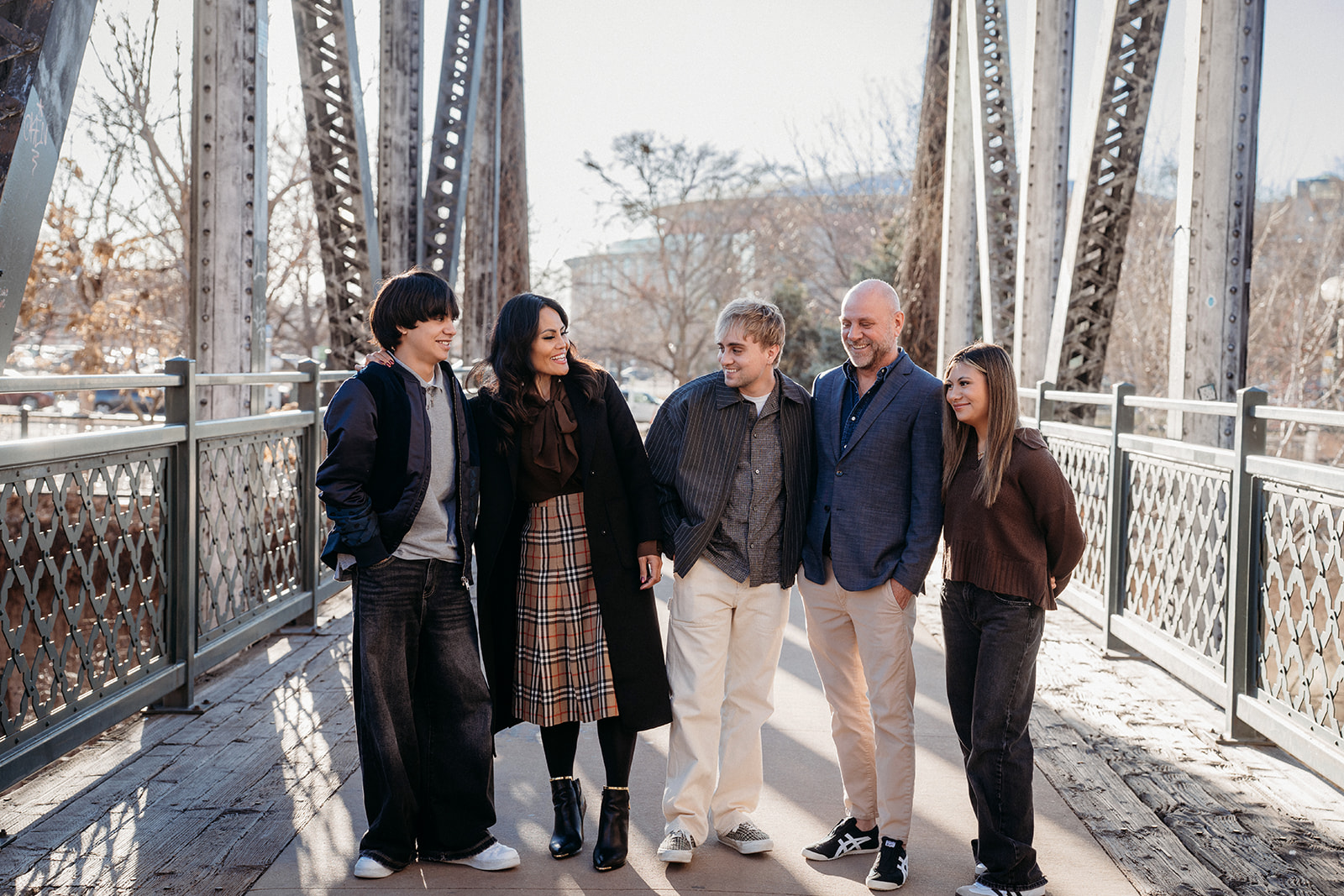 A family of five walking closely together across a steel bridge in Denver, sharing conversation and laughter during a session with Denver photographers.