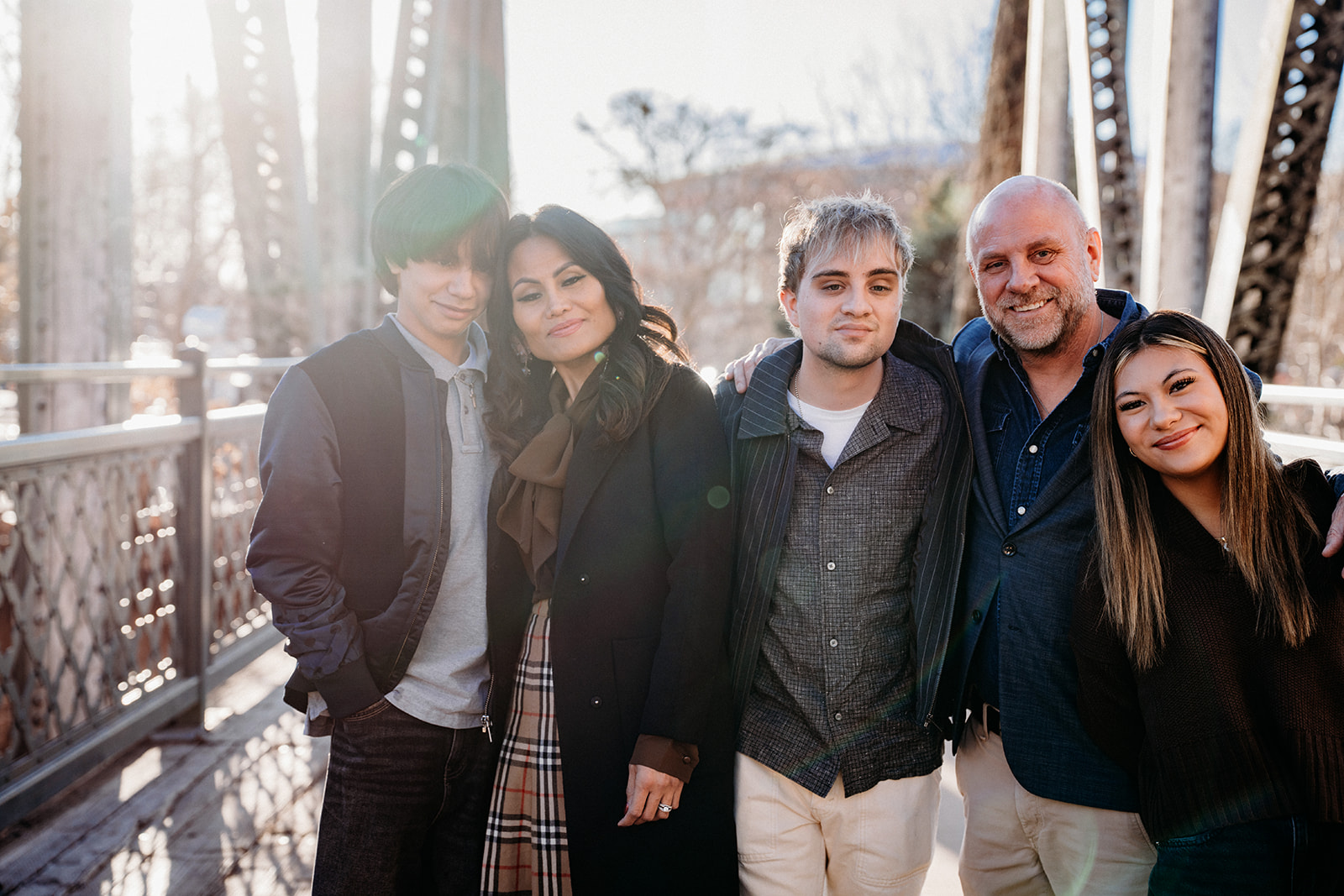 A family of five standing close together on a historic Denver bridge, smiling and relaxed during a winter family photo session with Denver photographers.