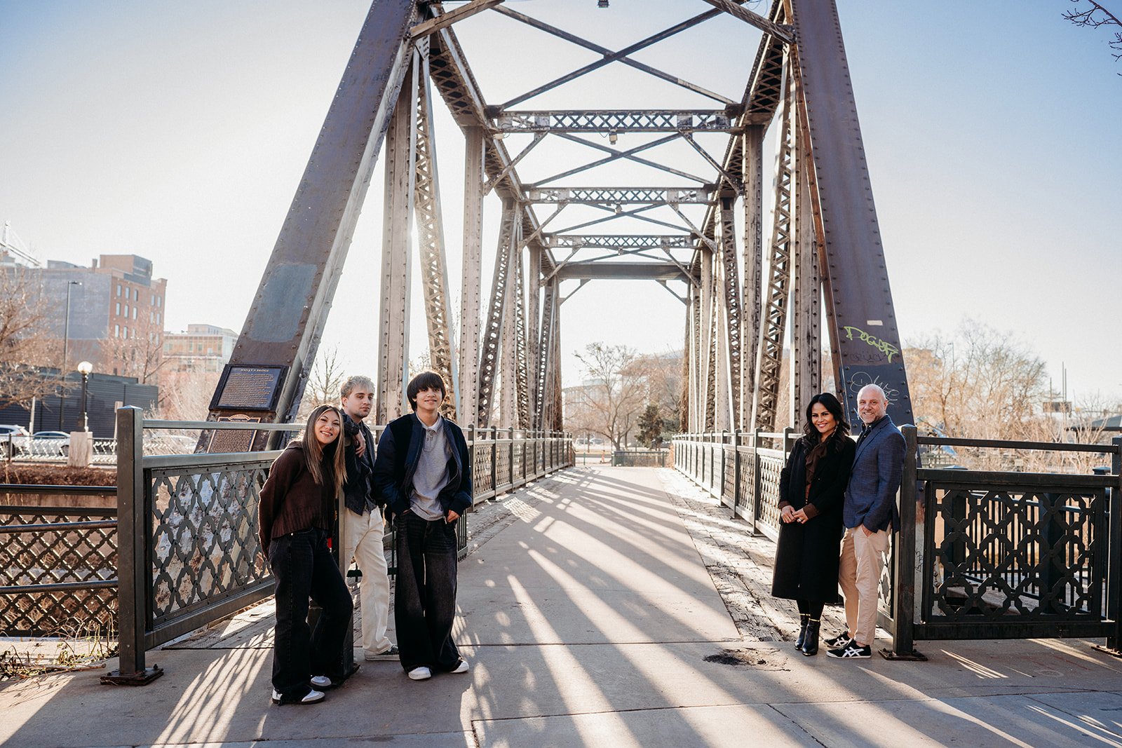 A family split into two groups on a historic Denver bridge, smiling and chatting during a relaxed lifestyle family photo session.