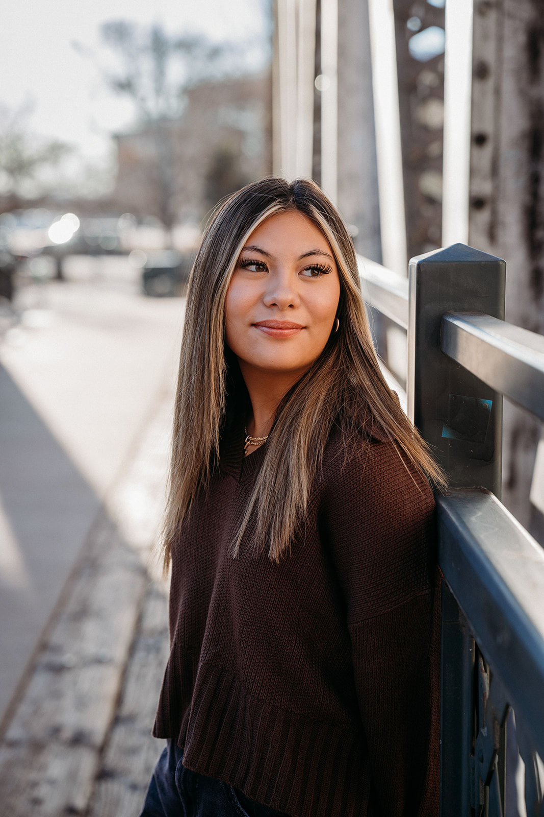 A young woman leaning against a bridge railing in Denver, looking off to the side during a natural light portrait session.