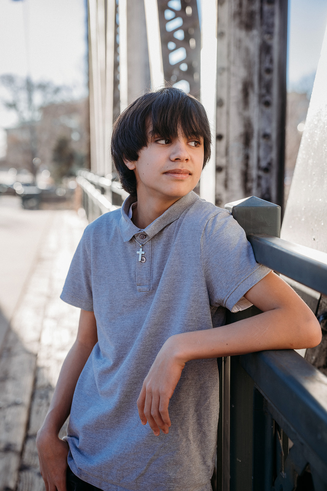 A teenage boy leaning on a bridge railing in Denver, looking off into the distance during a natural light portrait session with Denver photographers.