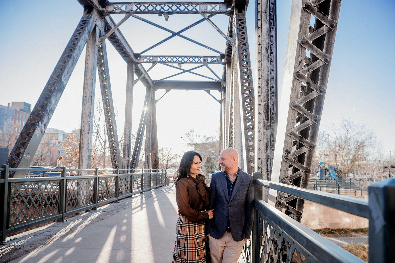A couple standing together on a Denver bridge, sharing a quiet moment and smiling at each other during a couples session with Denver photographers.