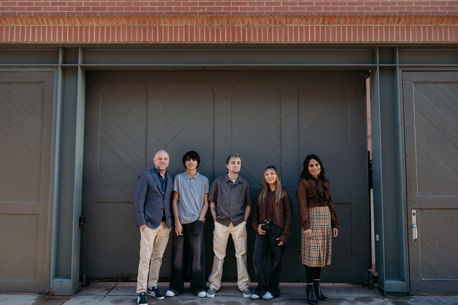 A family of five standing together in front of large industrial doors in downtown Denver during a relaxed family photo session with Denver photographers.